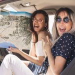 excited-woman-sitting-beside-her-friend-holding-map-car_23-2147855695