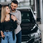 casal-jovem-escolhendo-um-carro-em-uma-sala-de-show-de-carro_1303-20284